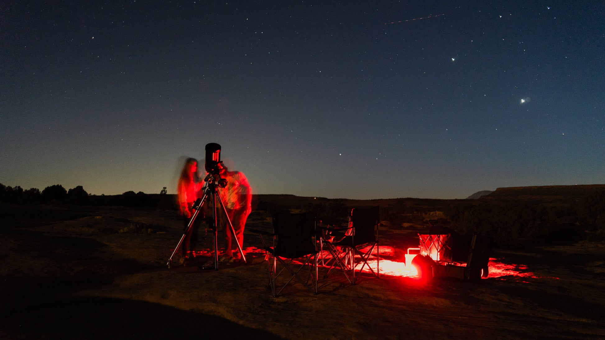 Two people observing the night sky with a telescope in a dark field.