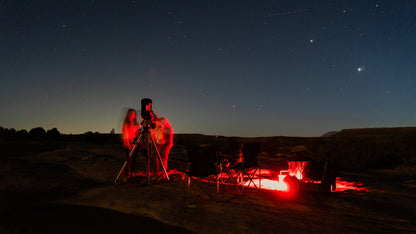 Two people observing the night sky with a telescope in a dark field.