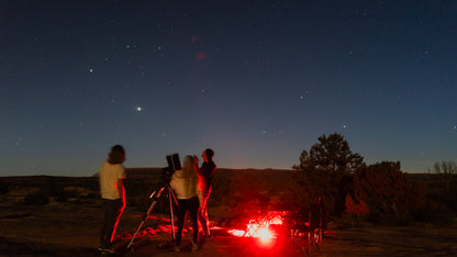 People observing the night sky with telescopes in a desert landscape.
