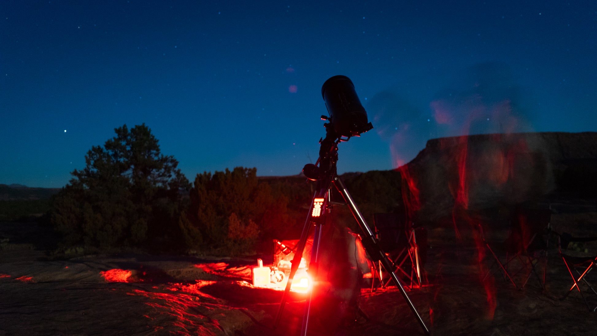 Telescope set up near a campfire at night with stars visible
