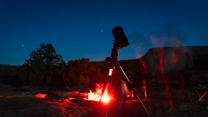 Telescope set up near a campfire at night with stars visible
