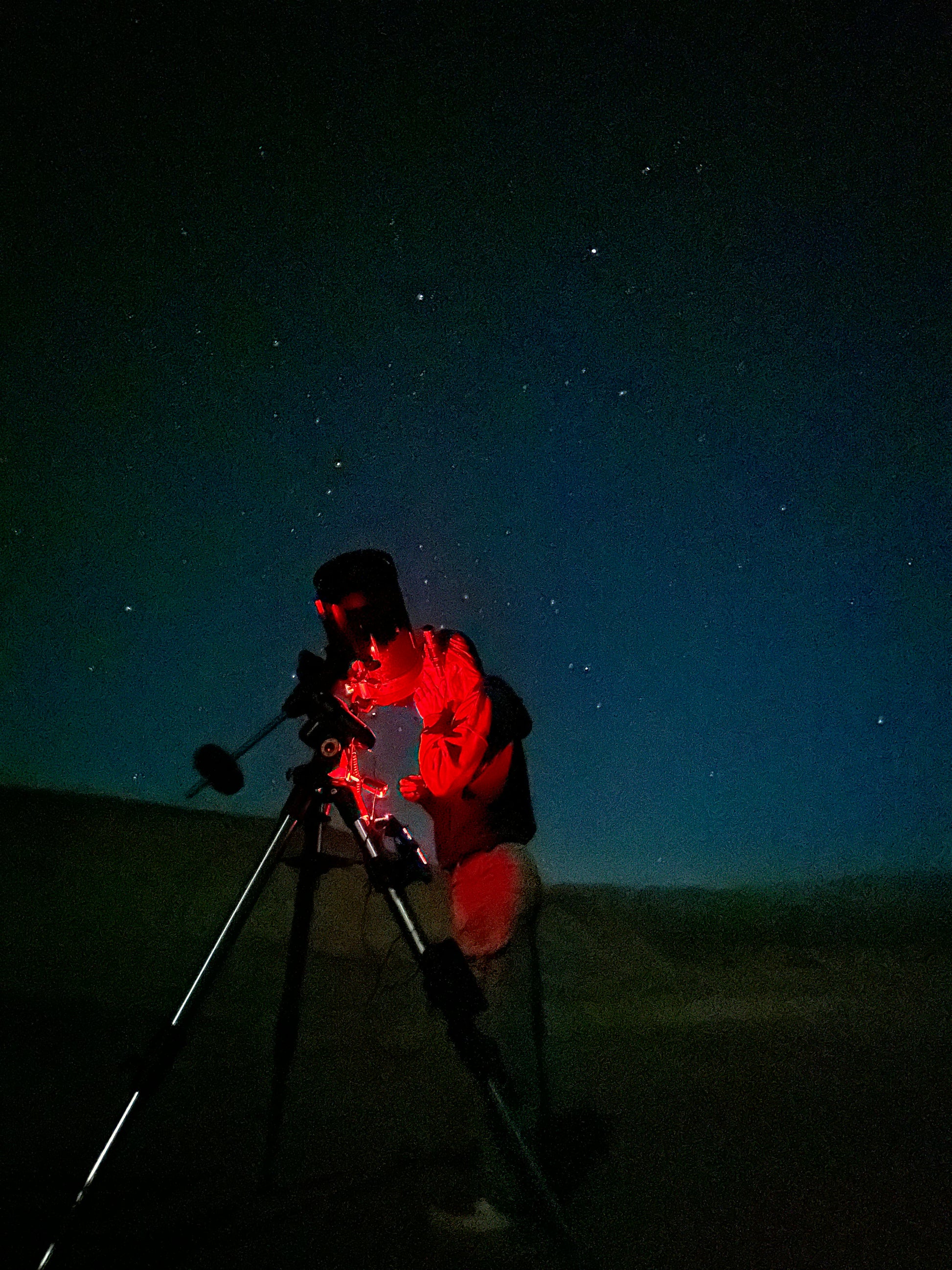 Person looking through a telescope with red light.
