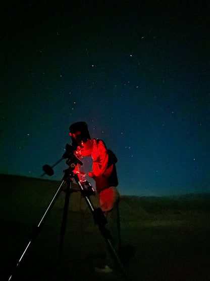 Person looking through a telescope with red light.