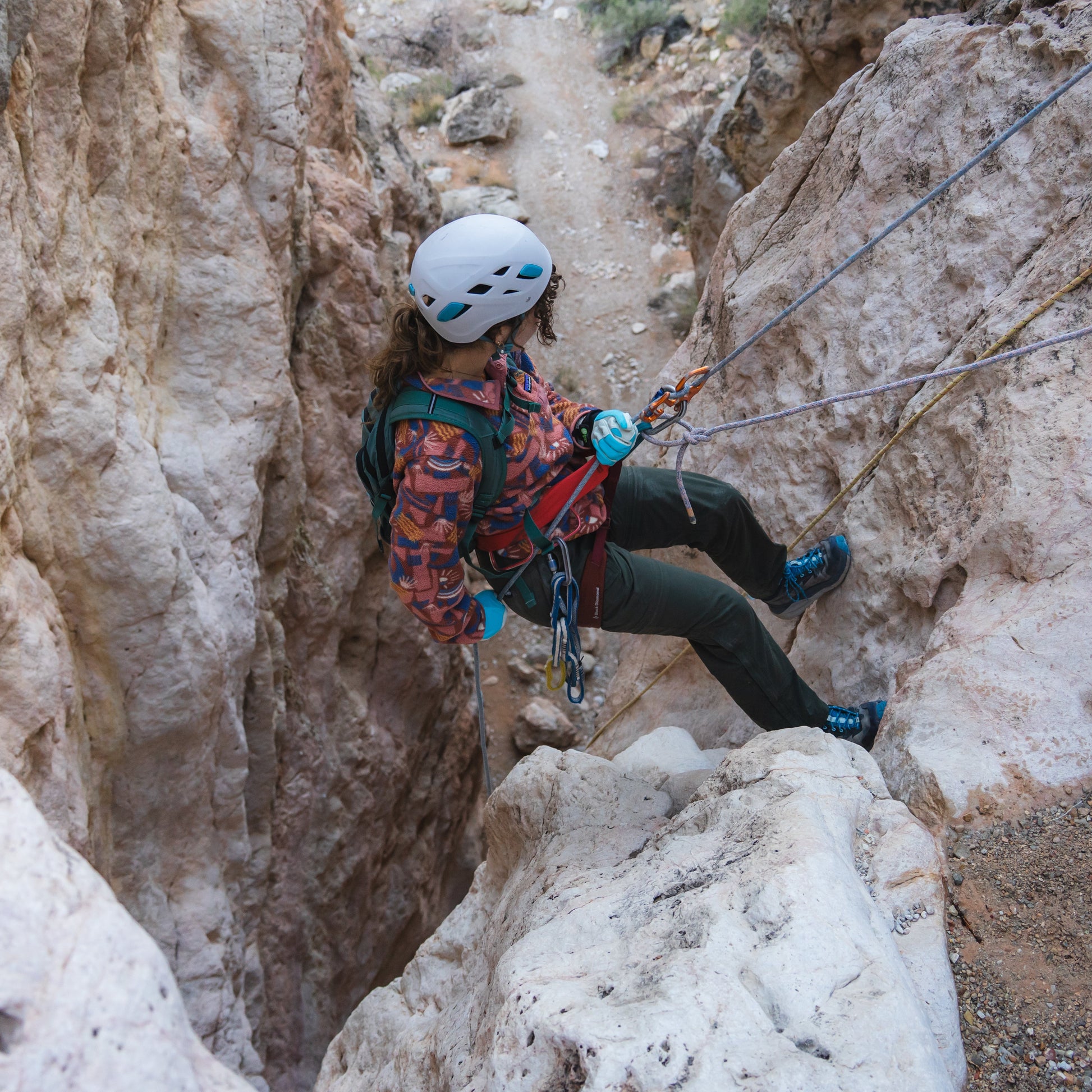Person climbing a rocky cliff using ropes and safety gear