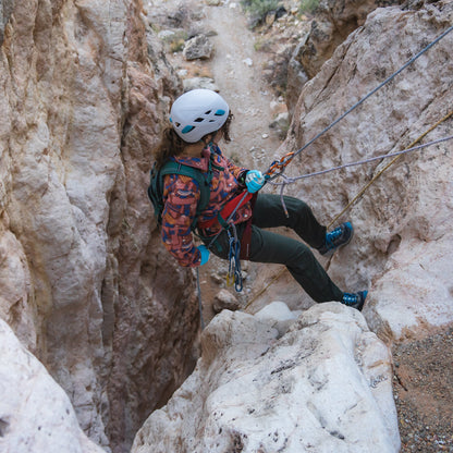 Person climbing a rocky cliff using ropes and safety gear