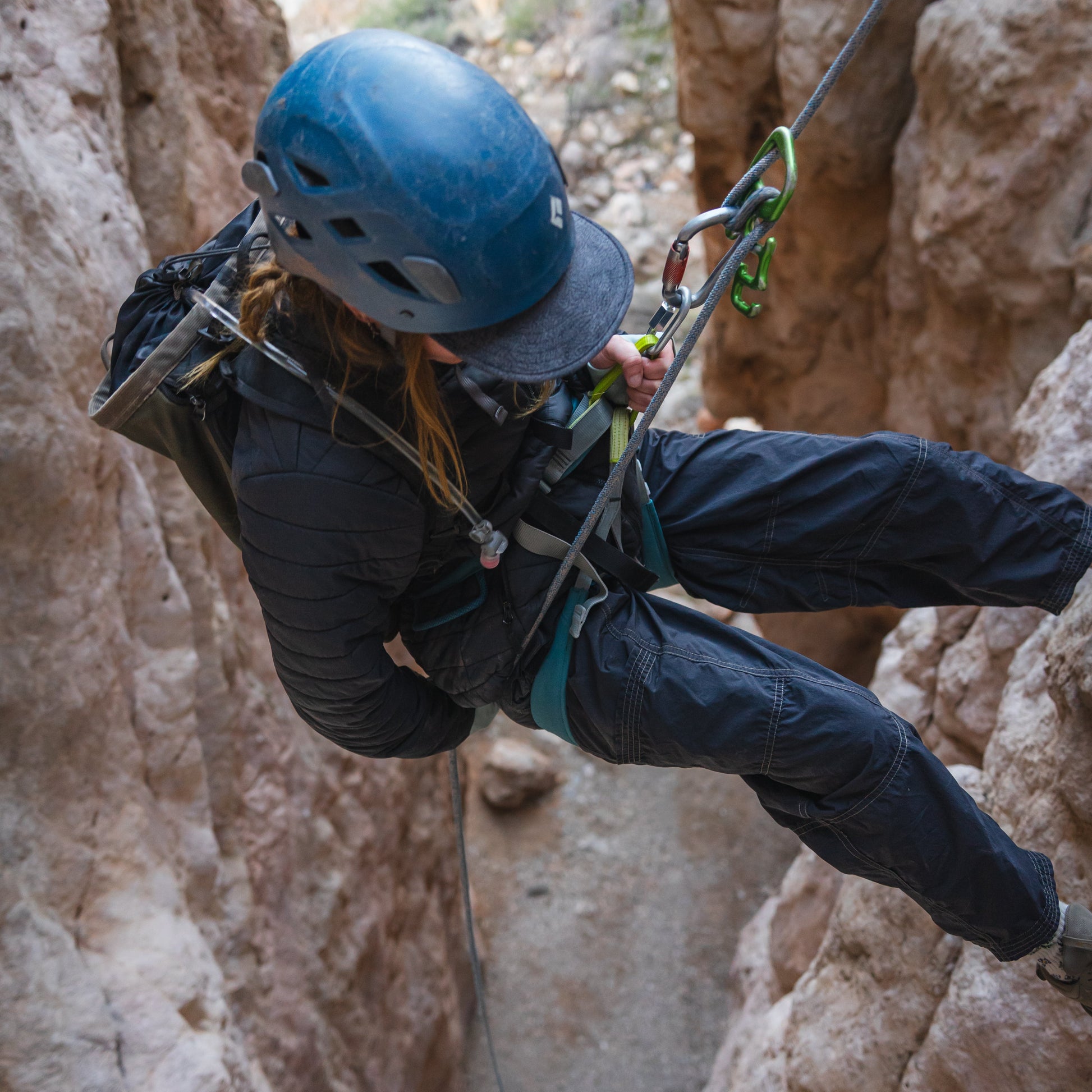Person rock climbing with a helmet and safety harness on a rocky cliff.