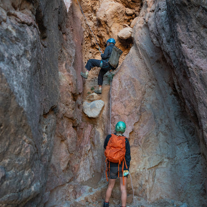 Two hikers with backpacks navigating a narrow rocky crevice.