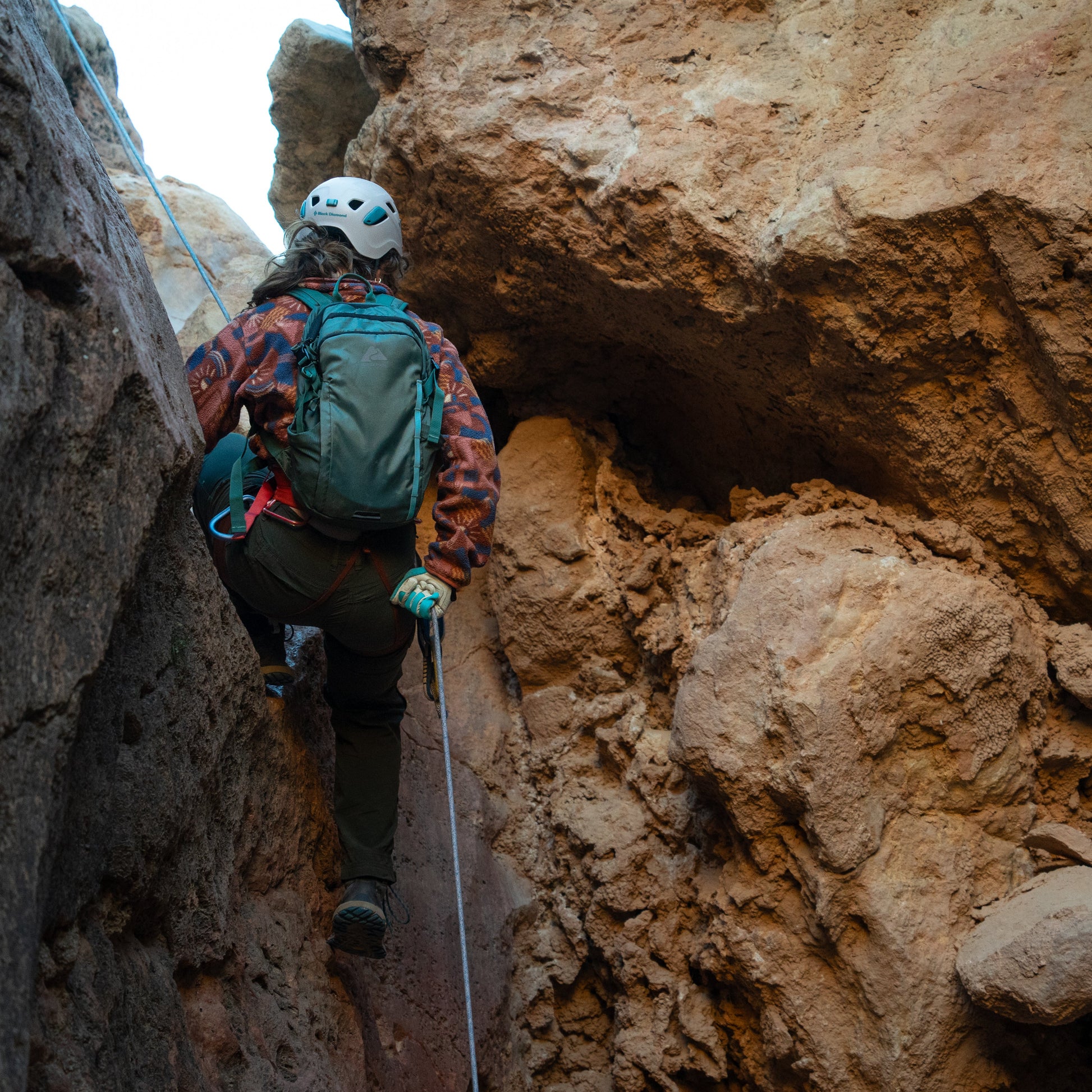 Person climbing through a narrow rocky passage with a helmet and backpack.