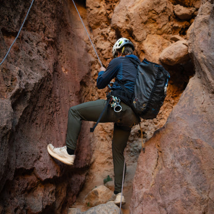 Person climbing a rocky cliff with a backpack and helmet