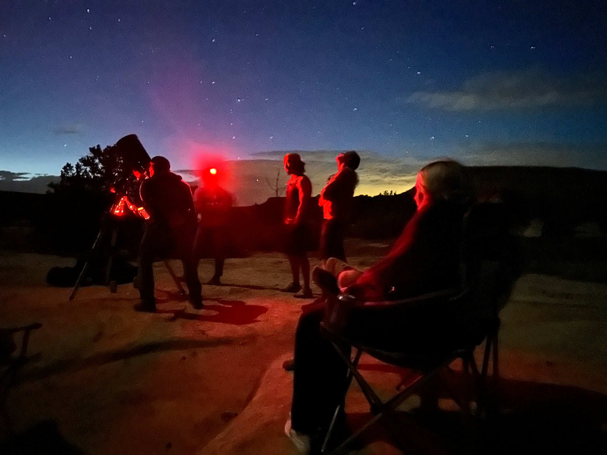 Group of people observing the night sky with a red light source in a desert setting.