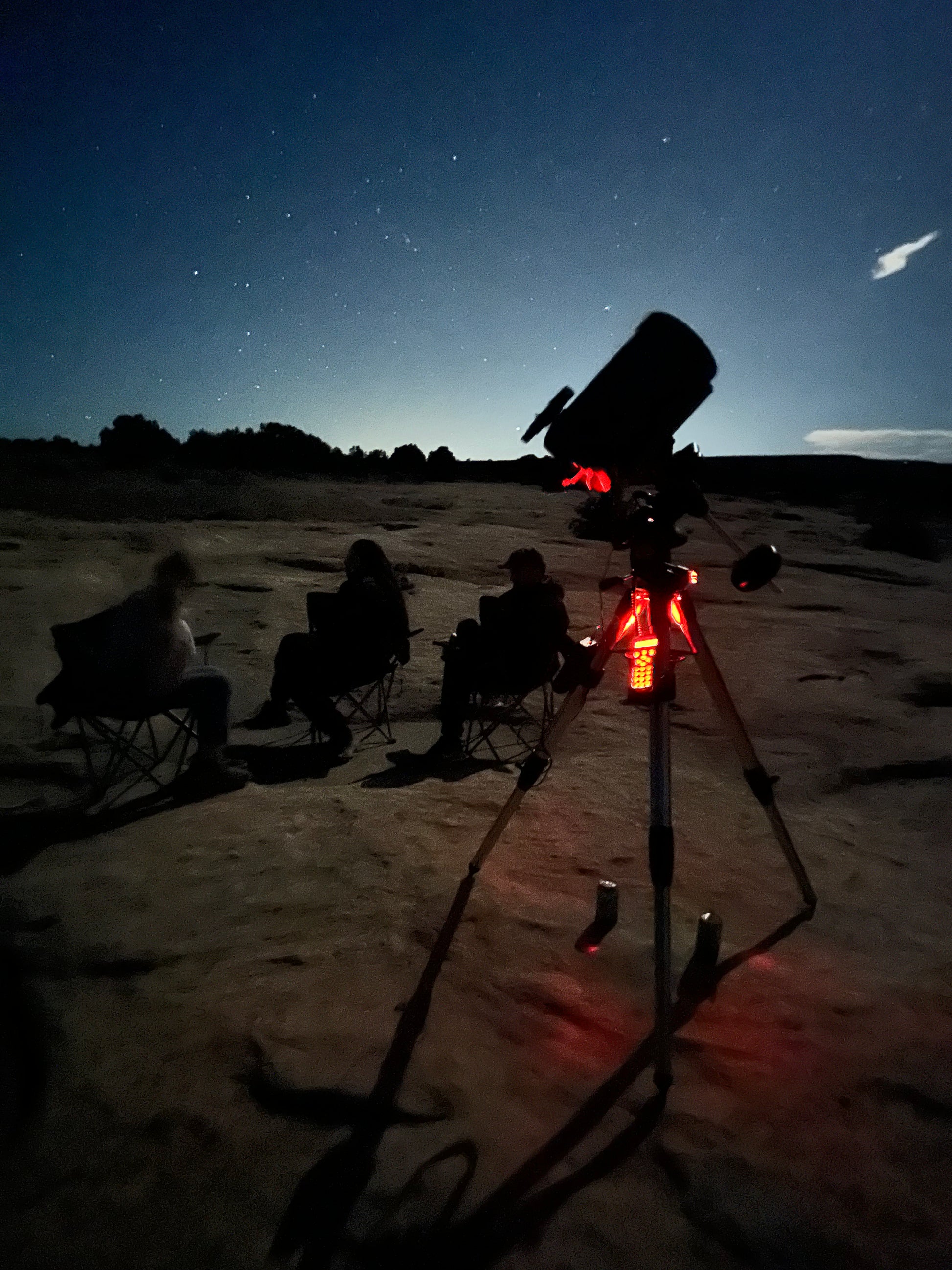 Telescope set up on a rocky plateau with a night sky and moon in the background