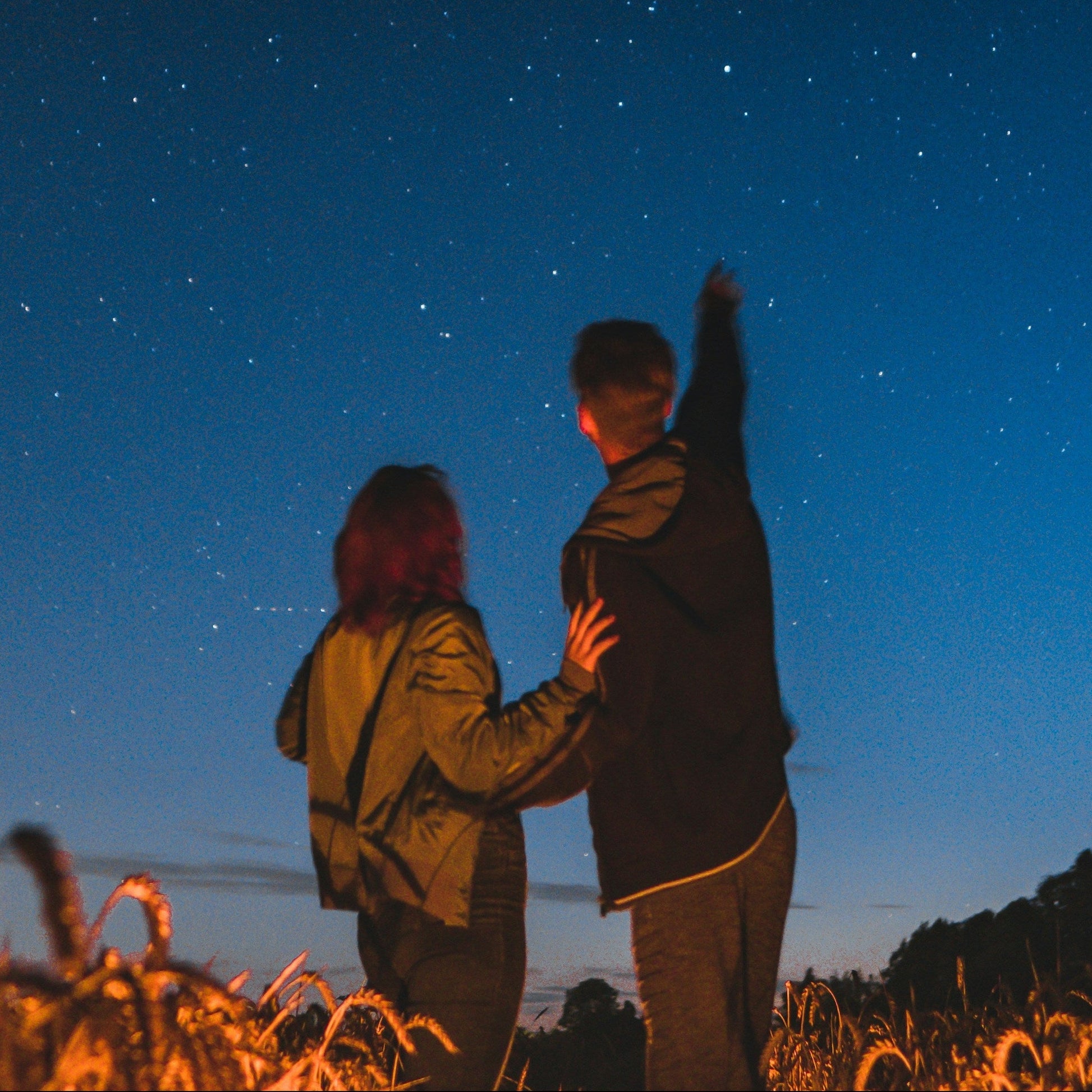 Two people standing in a field under a starry night sky.